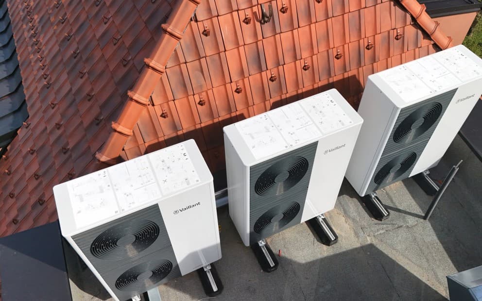 Außeneinheiten von Wärmepumpen, die vor einem Dach mit roten Ziegeln platziert sind.